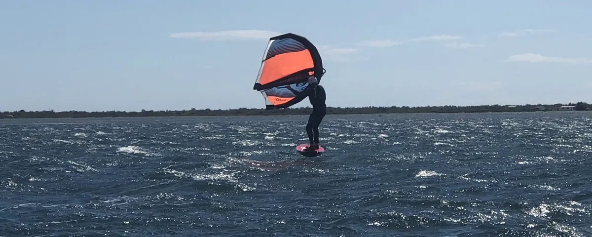 Pratiquant de wingfoil qui vole au-dessus de l'eau pendant un stage